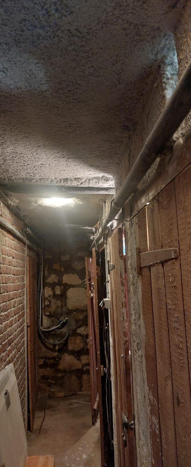 Couloir des caves au plafond recouvert d'isolant projeté, bordé de portes de caves en bois