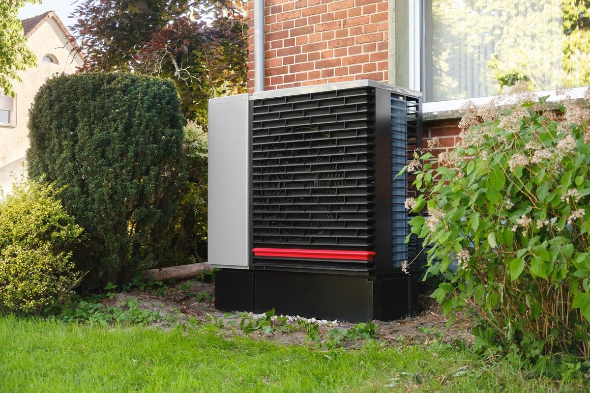 Unité extérieure d'une pompe à chaleur air/eau posée dans le jardin, devant une maison en briques